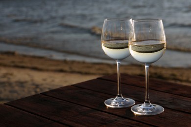 Photo of Two glasses of wine on wooden table near river at sunset. Space for text