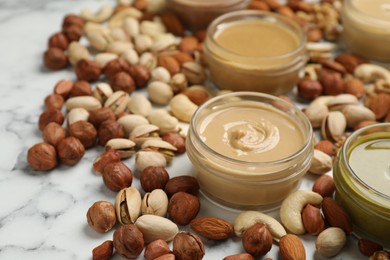 Photo of Jars with butters made of different nuts and ingredients on white marble table, closeup