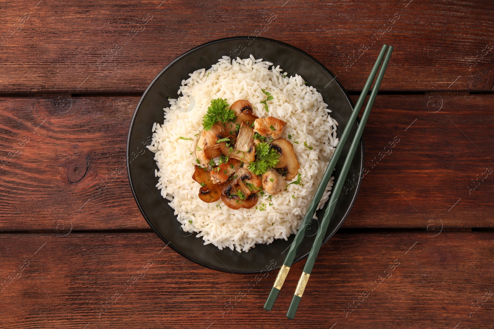 Photo of Delicious rice with mushrooms, parsley and chopsticks on wooden table, top view