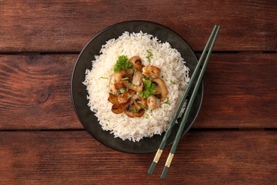 Delicious rice with mushrooms, parsley and chopsticks on wooden table, top view