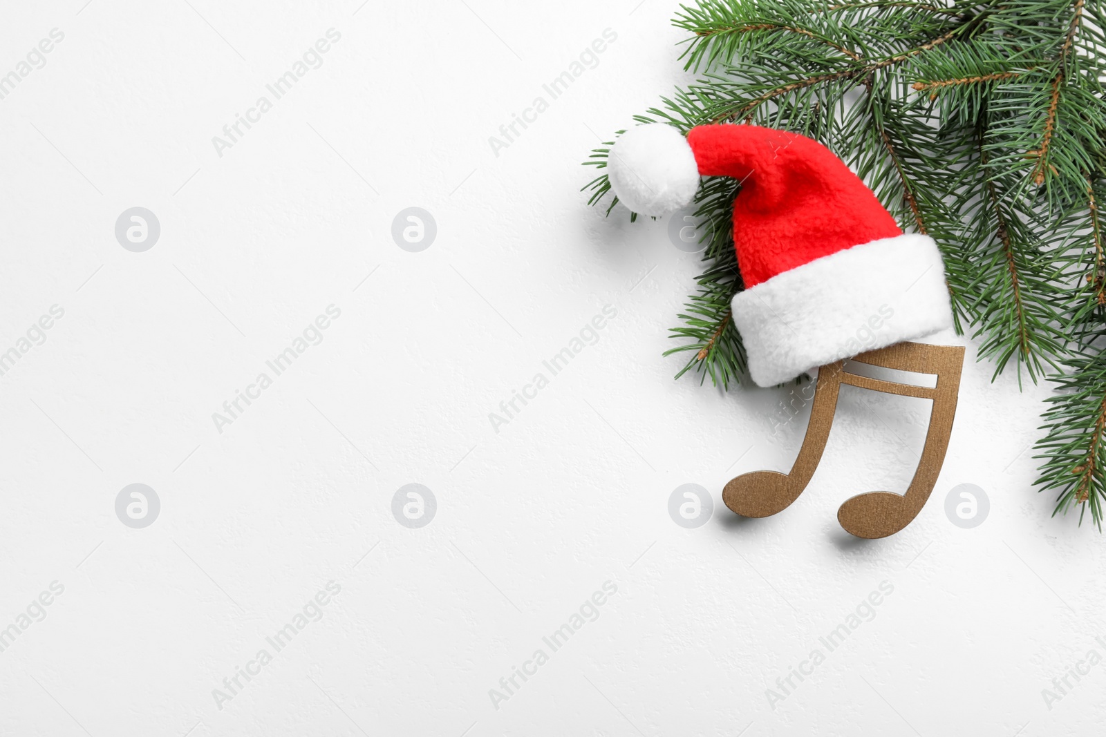 Photo of Decorative music note with Santa hat near fir tree branch and space for text on white wooden background, top view. Christmas celebration