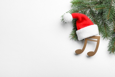 Photo of Decorative music note with Santa hat near fir tree branch and space for text on white wooden background, top view. Christmas celebration