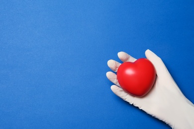 Photo of Doctor in medical glove holding heart on color background, top view. Space for text