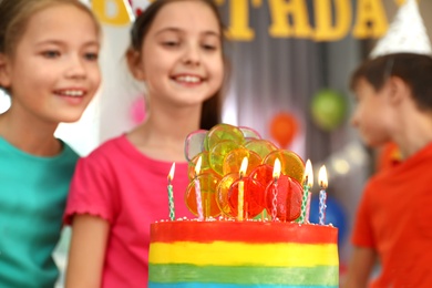 Children near cake with candles at birthday party indoors, closeup