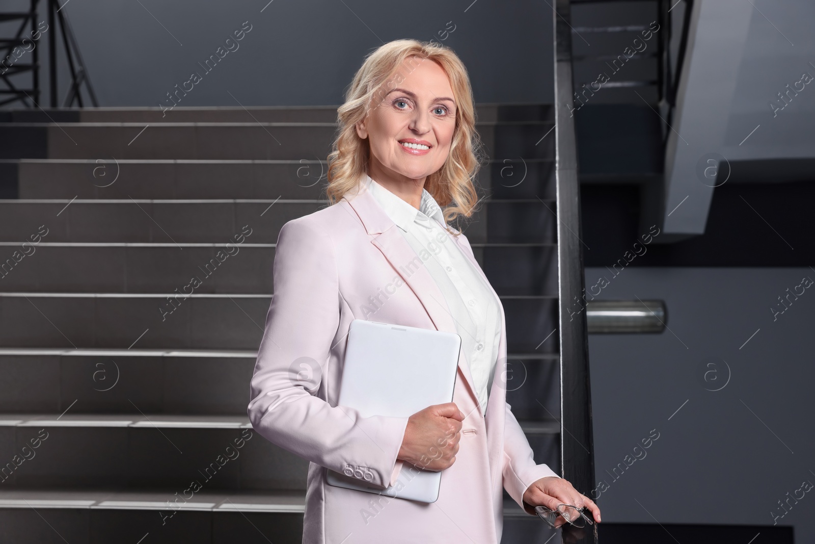 Photo of Happy lady boss with tablet near staircase indoors. Successful businesswoman