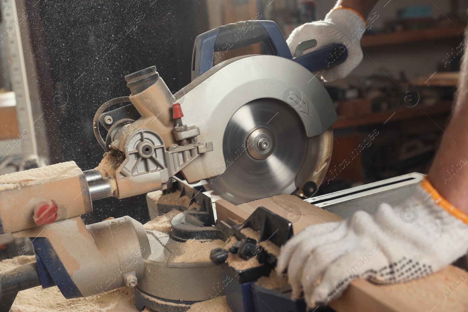 Photo of Professional carpenter cutting wooden planks with sawmill in workshop, closeup