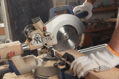 Photo of Professional carpenter cutting wooden planks with sawmill in workshop, closeup