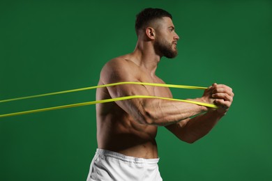 Photo of Muscular man exercising with elastic resistance band on green background