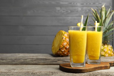 Photo of Tasty pineapple smoothie and cut fruit on wooden table, space for text