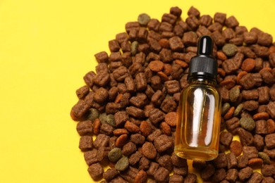 Photo of Top view of tincture in glass bottle and dry pet food on yellow background, closeup