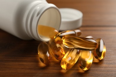 Photo of Overturned bottle with dietary supplement capsules on wooden table, closeup