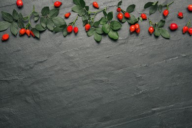 Ripe rose hip berries with green leaves on black table, flat lay. Space for text