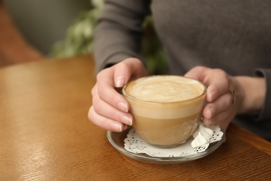 Photo of Young woman with cup of delicious coffee at table