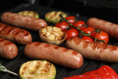 Cooking delicious fresh sausages with vegetables on modern grill, closeup