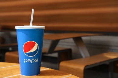 Photo of MYKOLAIV, UKRAINE - JUNE 9, 2021: Paper Pepsi cup on wooden table outdoors