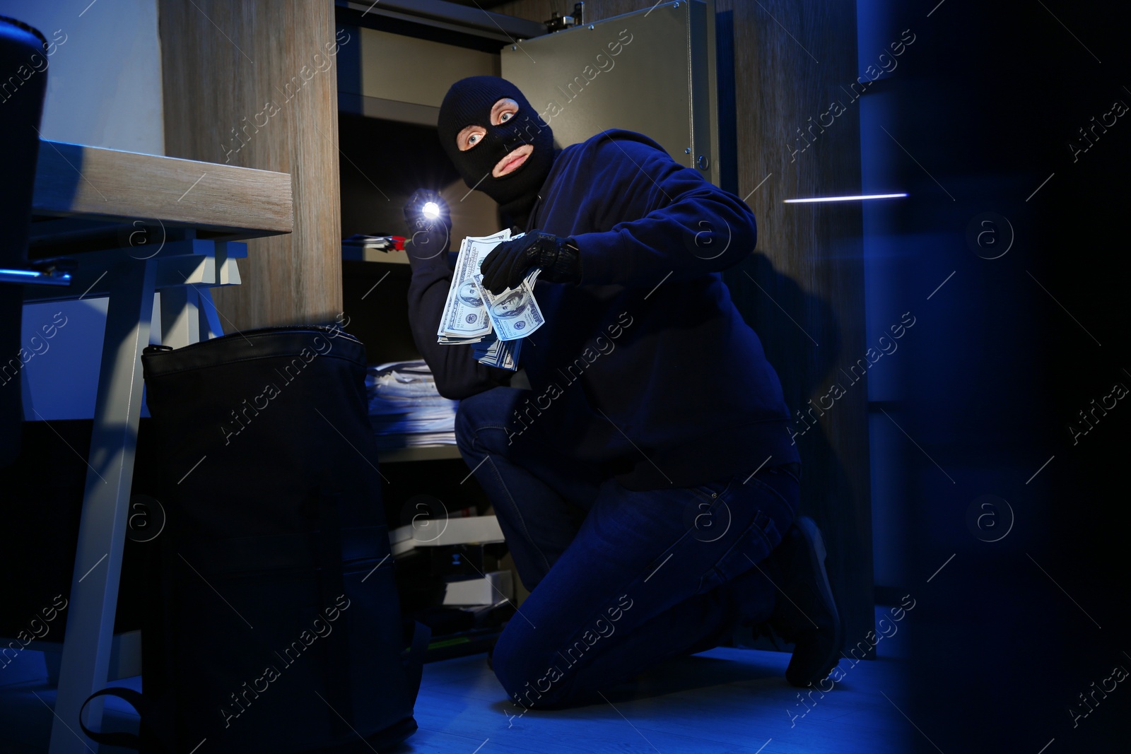 Photo of Thief taking money out of steel safe indoors at night