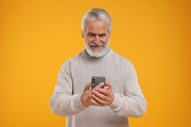 Photo of Happy senior man using smartphone on yellow background