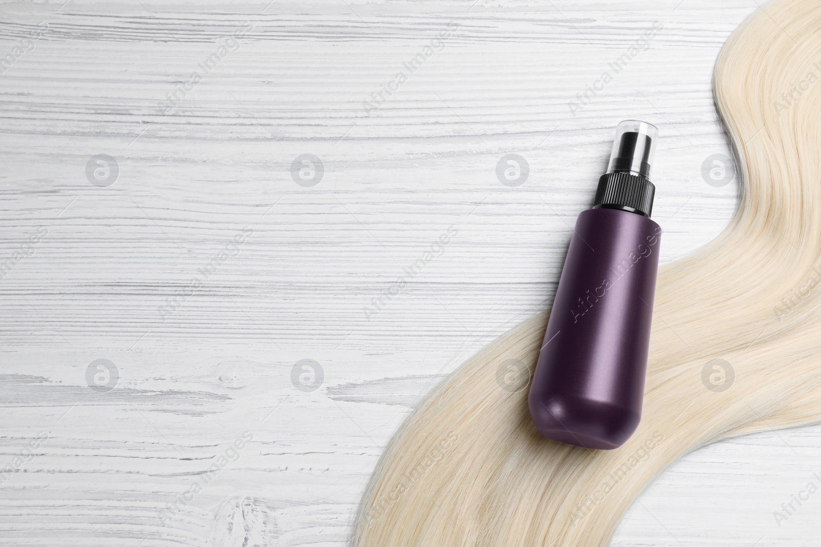 Photo of Spray bottle with thermal protection and lock of blonde hair on white wooden table, flat lay. Space for text