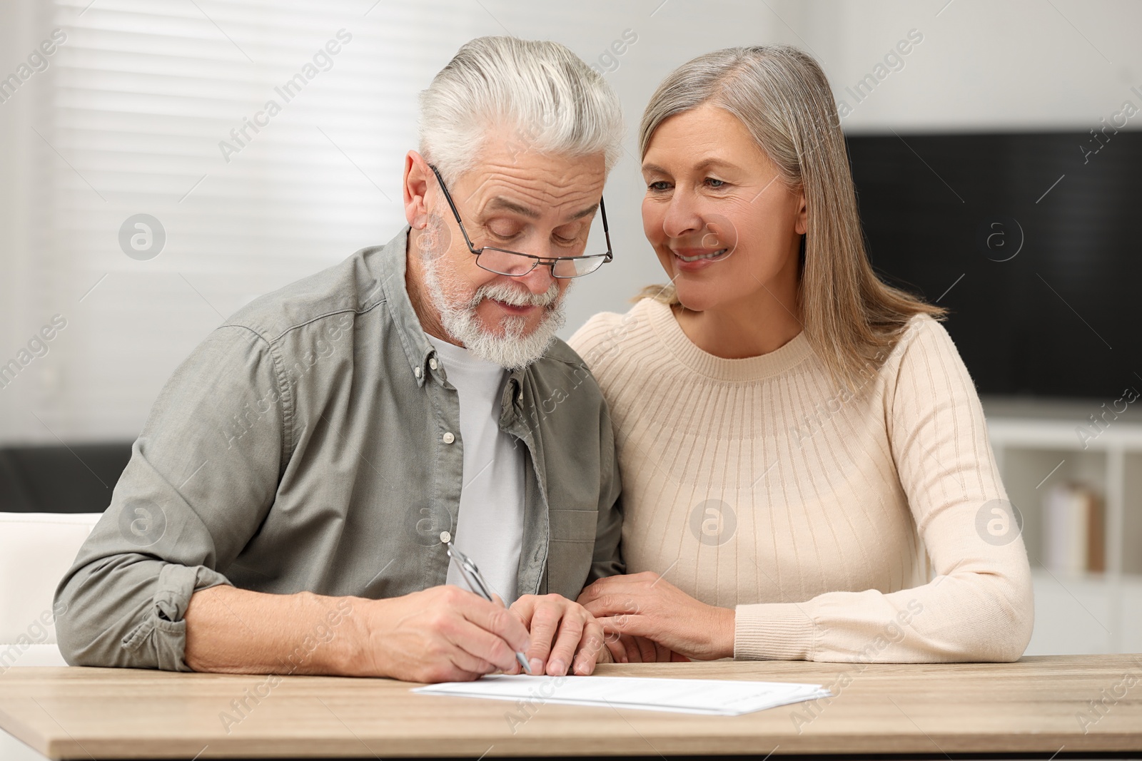 Photo of Senior couple signing Last Will and Testament indoors