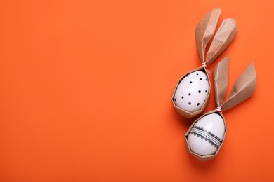 Photo of Easter bunnies made of craft paper and eggs on orange background, flat lay. Space for text