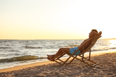 Young man relaxing in deck chair on beach near sea