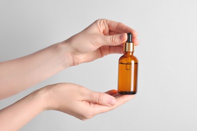 Photo of Woman holding bottle of cosmetic oil on light background, closeup