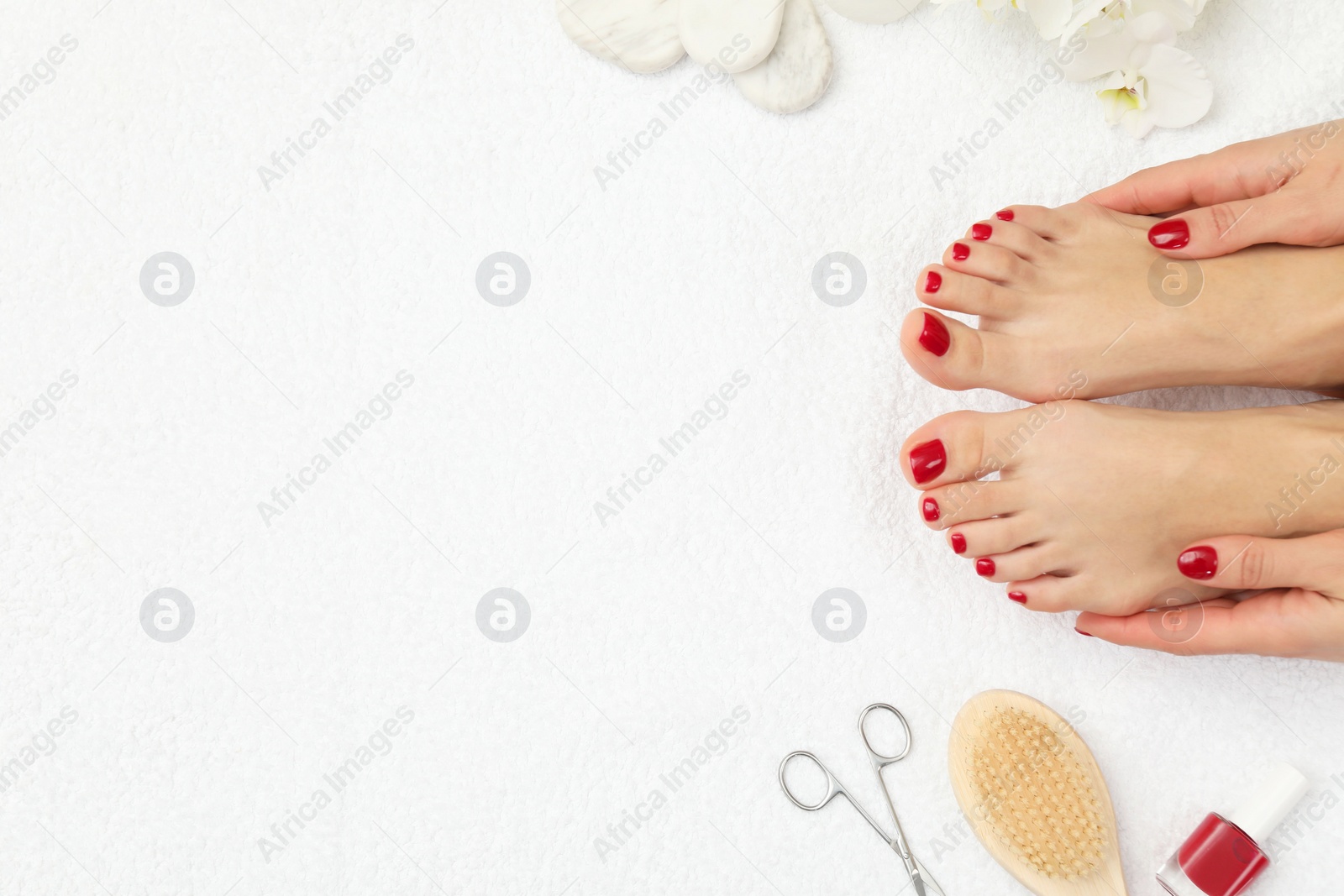 Photo of Woman with stylish red toenails after pedicure procedure and orchid flowers on white terry towel, top view. Space for text