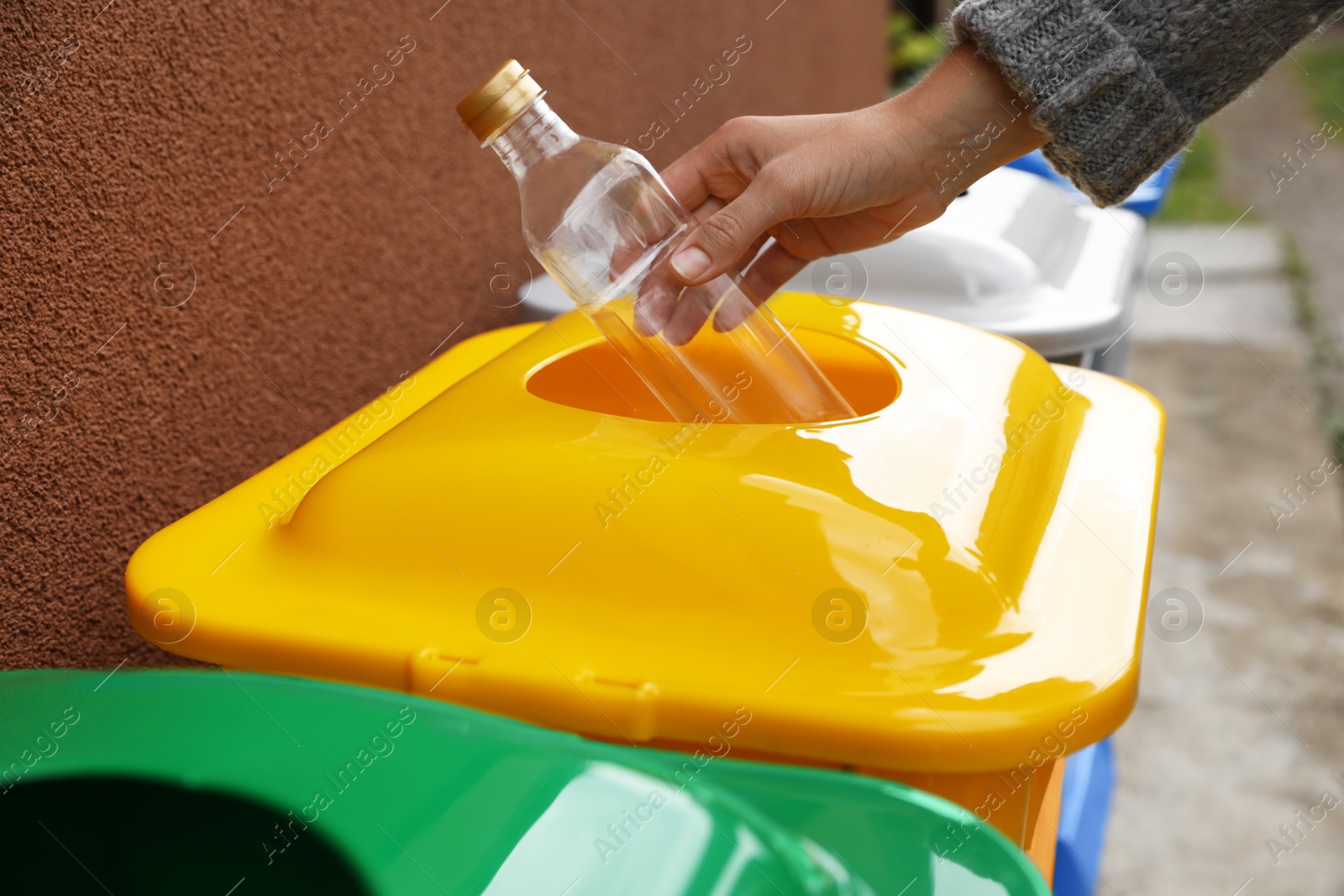 Photo of Woman throwing bottle into recycling bin outdoors, closeup