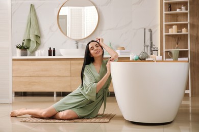 Photo of Beautiful young woman sitting near tub in bathroom