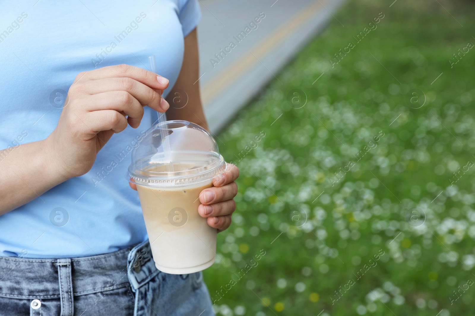 Photo of Woman holding plastic takeaway cup of delicious iced coffee outdoors, closeup. Space for text