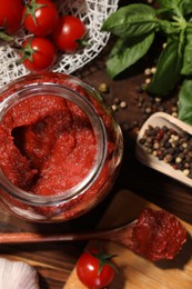 Jar of tasty tomato paste and ingredients on wooden table, flat lay