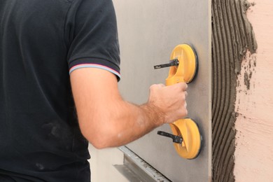 Photo of Worker using suction plate for tile installation indoors, closeup