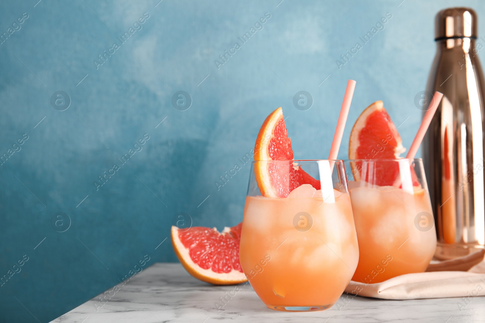 Photo of Glasses of grapefruit cocktails served on table against color background. Space for text