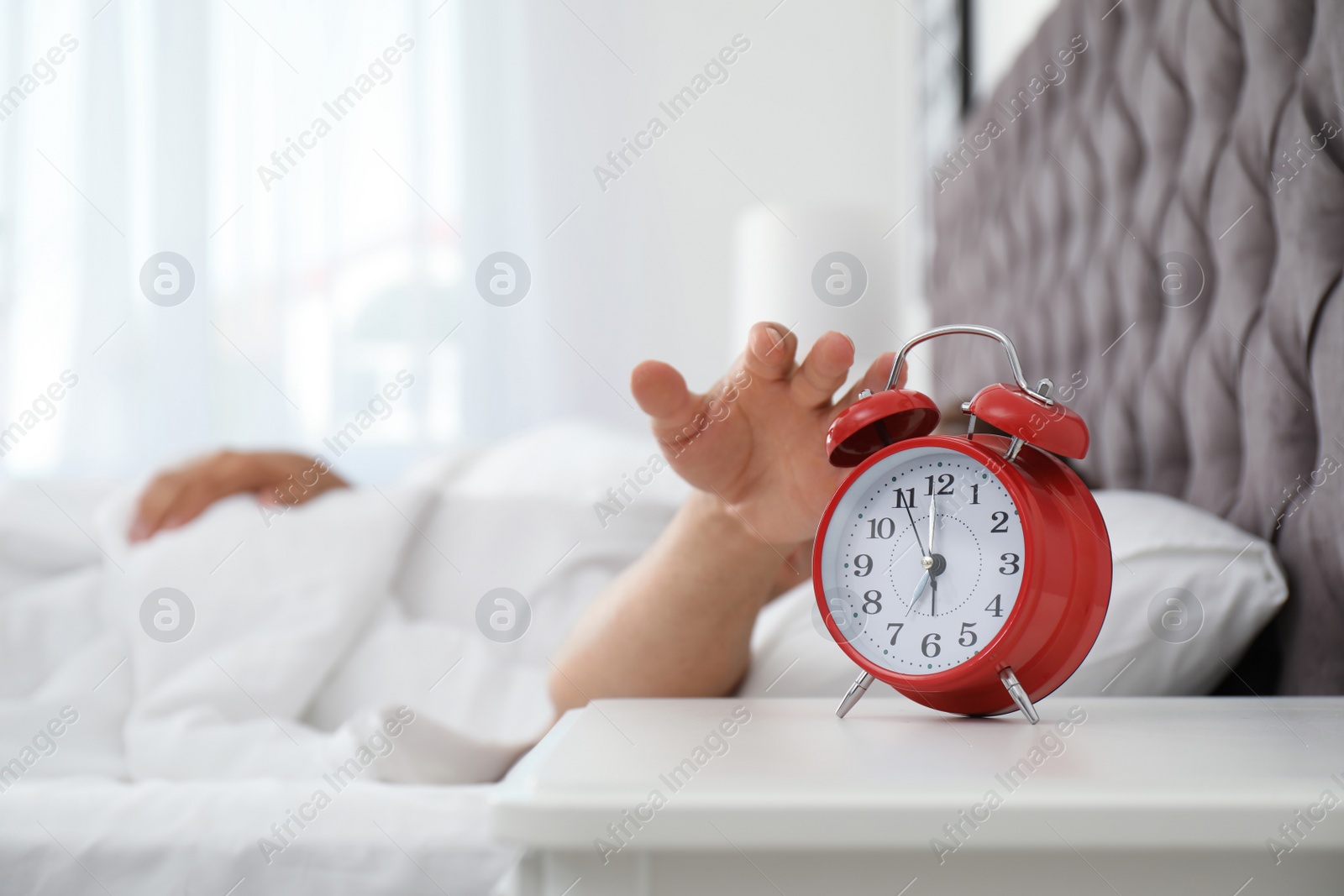 Photo of Man turning off alarm clock in bedroom