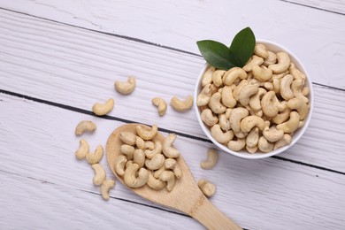 Photo of Tasty cashew nuts and green leaves on white wooden table, flat lay