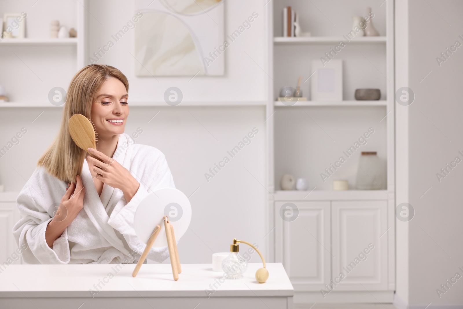 Photo of Beautiful woman brushing her hair at vanity in room. Space for text