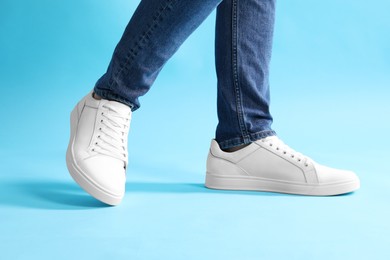 Photo of Man wearing stylish white sneakers on light blue background, closeup