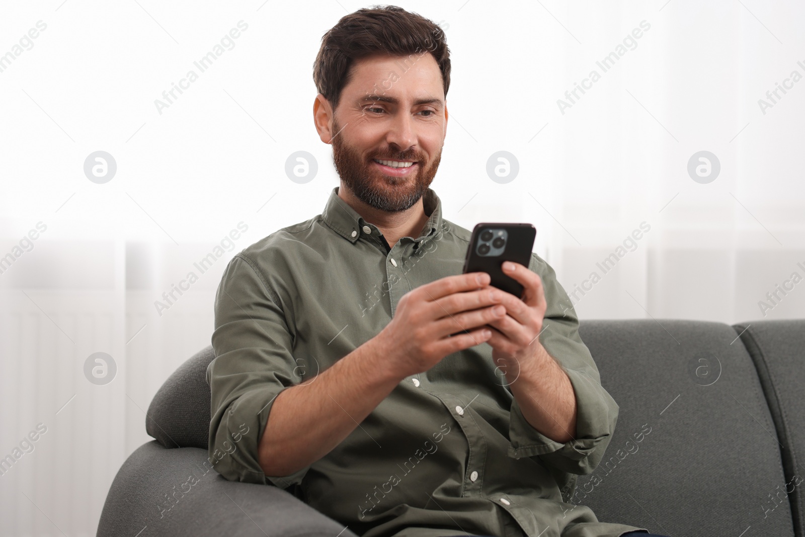 Photo of Smiling man using smartphone on sofa at home