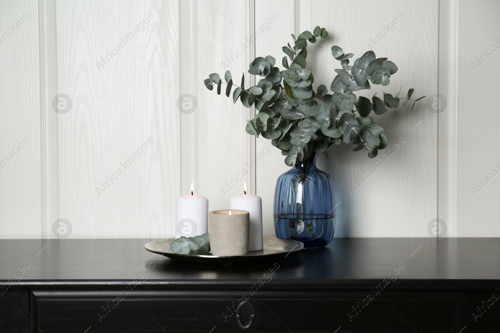 Photo of Eucalyptus branches and burning candles on black table