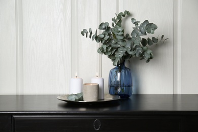 Eucalyptus branches and burning candles on black table