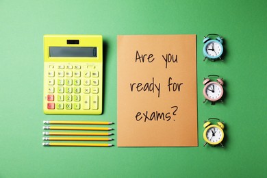 Photo of Flat lay composition with question Are you ready for exams, alarm clocks , calculator and pencils on green background