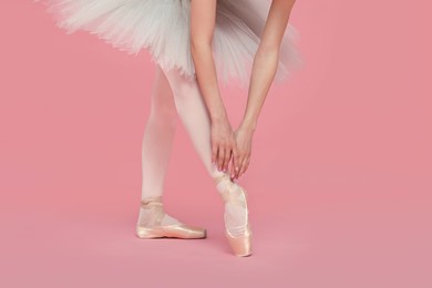 Photo of Young ballerina in pointe shoes practicing dance moves on pink background, closeup