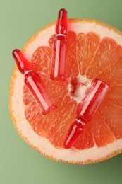 Skincare ampoules with vitamin C and half of grapefruit on light green background, top view