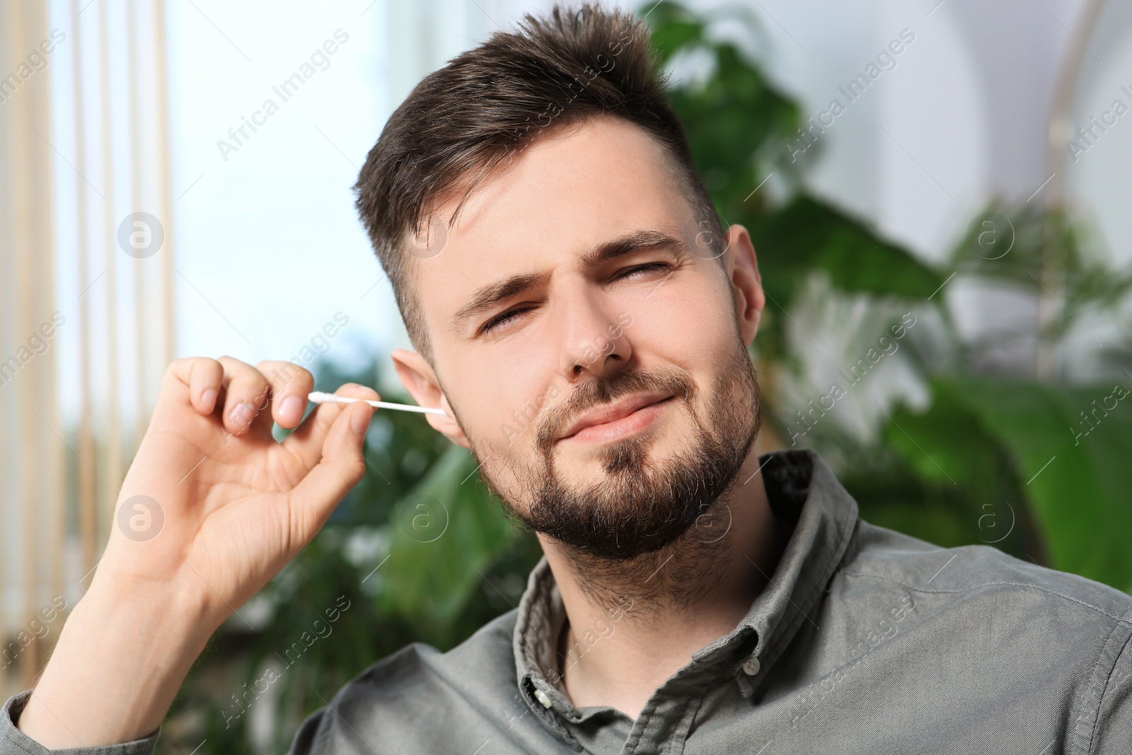 Photo of Young man cleaning ear with cotton swab at home