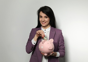 Photo of Businesswoman putting money into piggy bank on light background