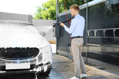 Photo of Businessman cleaning auto with high pressure water jet at self-service car wash