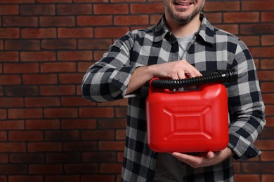 Man holding red canister against brick wall, closeup. Space for text