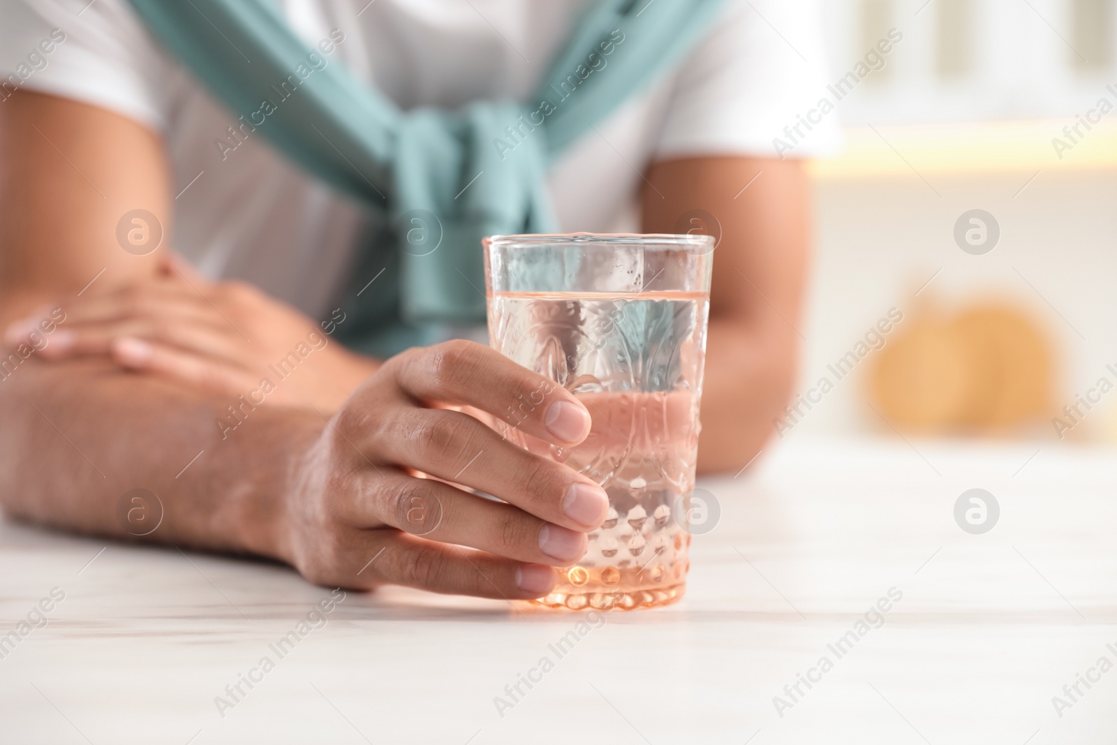 Photo of Man holding glass of pure water at table in kitchen, closeup