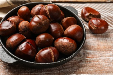 Photo of Fresh edible sweet chestnuts in frying pan on wooden table, closeup