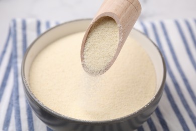 Photo of Pouring uncooked organic semolina from scoop into bowl, closeup